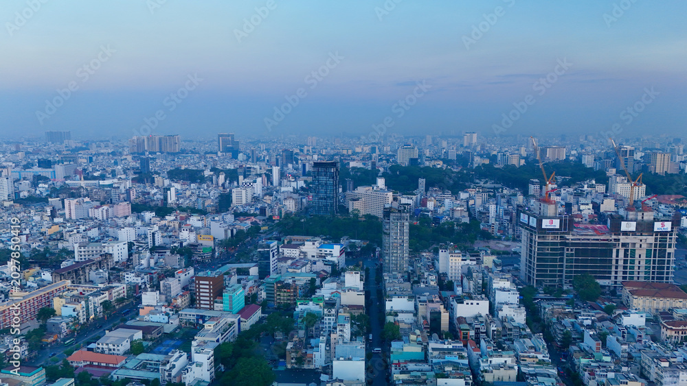 Fototapeta premium Ho Chi Minh City, Vietnam – 4K aerial sunrise drone view of downtown skyline with modern skyscrapers, dense urban housing, busy streets and morning traffic along the Saigon River in Southeast Asia