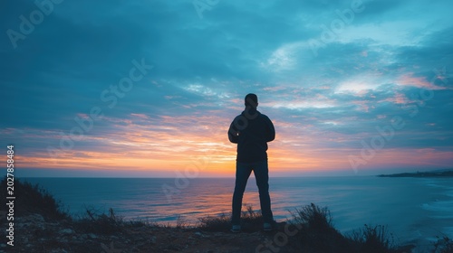 Solitude at Sunset: A lone figure stands silhouetted against a vibrant sunset, gazing out at the vast expanse of the ocean, embodying a moment of contemplation and peace.