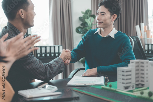 The real estate agent hands over the house model to the client after they sign a handshake over the model, symbolizing the completion of the real estate transaction.