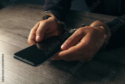 Bilde på lerret A close-up of a man's handcuffed hands holding a phone on a wooden table