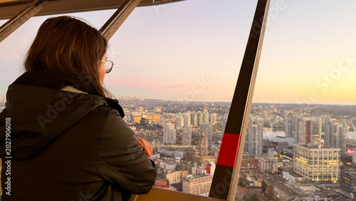 Woman gazing at Vancouver cityscape from Vancouver Tower observation deck at sunset