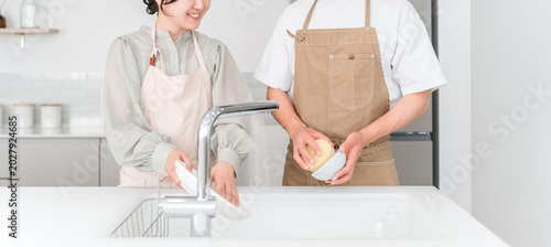A close-knit Asian couple chatting while doing household chores and washing dishes together in the kitchen of their home.