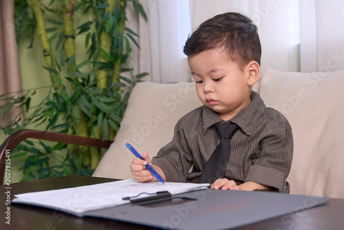 A 2-year-old baby boy sitting on the sofa writing with a blue pen