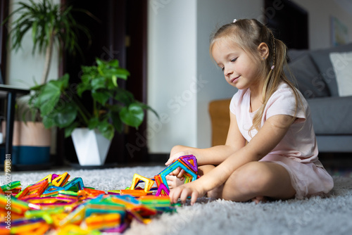 Young girl playing with colorful magnetic building tiles on a carpet in a living room