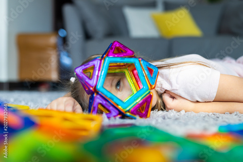 Young girl playing on the floor with colorful magnetic building blocks