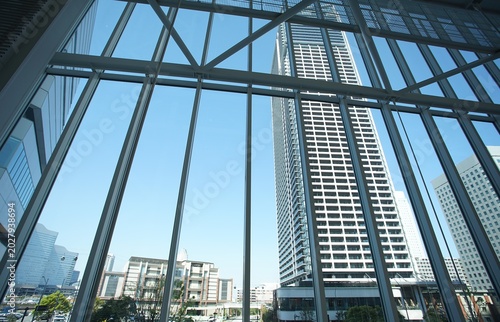 A view from inside a building looking through large floor-to-ceiling windows at neighboring high-rise architecture under a clear blue sky