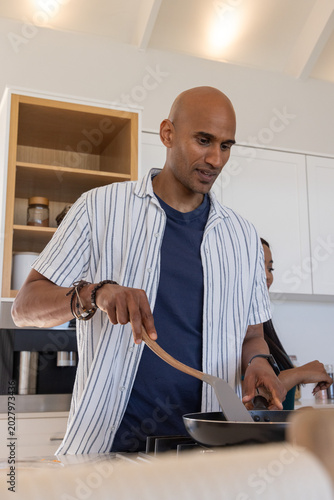 Couple cooking at stovetop in modern kitchen with frying pan and wooden spatula wearing bracelets