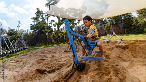 Foto Cute Asian boy playing with sand excavator toy in outdoor playground sandbox
