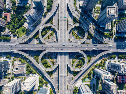 Aerial view of a complex urban cloverleaf interchange with multiple highway lanes and city skyscrapers in a modern metropolitan environment.