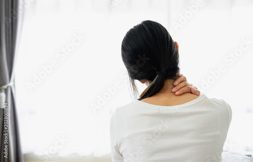 Back view of woman holding neck in pain at home. Healthcare, muscle tension, office syndrome and body pain concept with copy space.