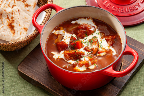 Foto Beef stew or curry with fresh cream topping in a red cast iron pot, served with