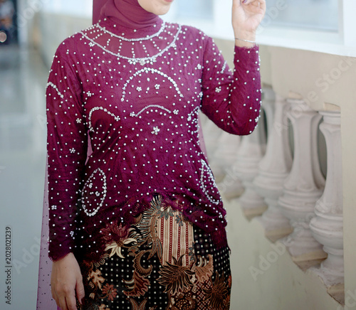 Faceless female body wearing a luxurious burgundy kebaya with beautiful batik cloth