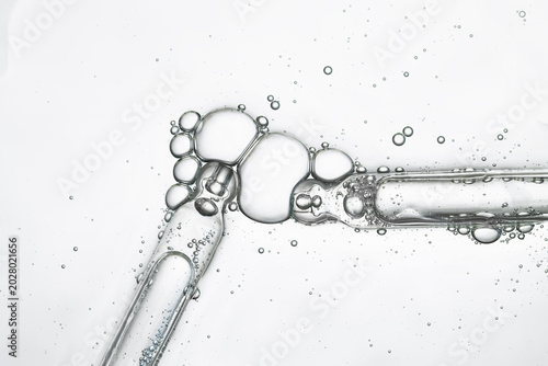 Two pipettes with bubbles of transparent cosmetic product, close-up, top view.
