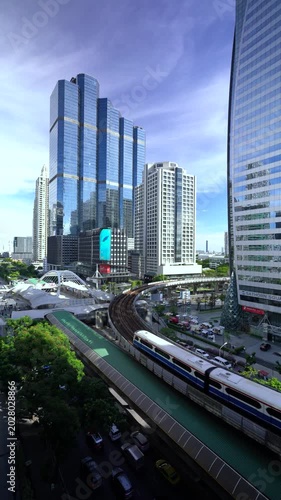 High-angle time-lapse of a BTS Skytrain navigating a dramatic curved track surrounded by modern skyscrapers and corporate office buildings at the Chong Nonsi intersection in Sathorn, Bangkok, Thailand