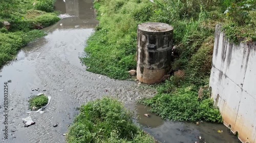 Panoramic View shows Overgrown Drainage Canal Surrounded by Wild Vegetation Near Quiet Bridge