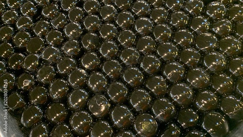 Glossy black tapioca pearls, often referred as giant boba pearls on aluminum tray, infused with flavors like brown sugar or caramel to enhance their taste. commonly used in specialty bubble tea drinks