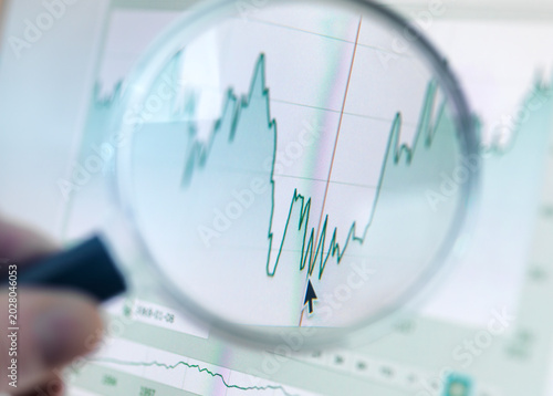 Investor analysing line graph on computer screen with magnifying glass
