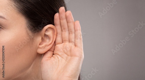 Close-up of woman with hand cupped behind her ear indicating listening or curiosity in neutral setting