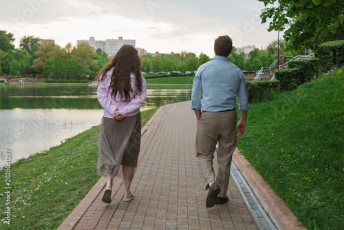 Photos Distant couple walks apart along lakeside park path in spring city landscape, ex