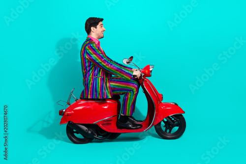 Colorful showman rides a red scooter against a turquoise studio background