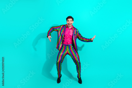 Vibrant showman in rainbow suit jumps for joy on teal backdrop at dynamic party performance