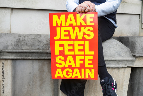 London, UK, Thousands of people gathered outside Downing Street for a protest against antisemitism. Person holding a bright red protest sign with yellow text saying Make Jews feel safe again.