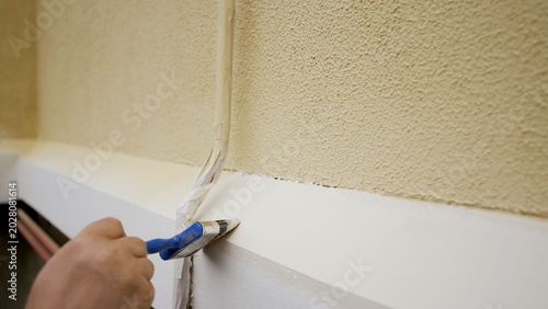 Εκτύπωση καμβά Close up of a painter's hand applying fresh white paint to an exterior house ledge with a brush