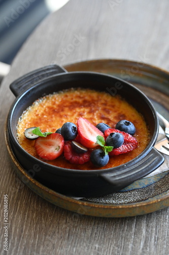 Fotografie French crème brûlée dessert with fresh fruit served in a black bowl