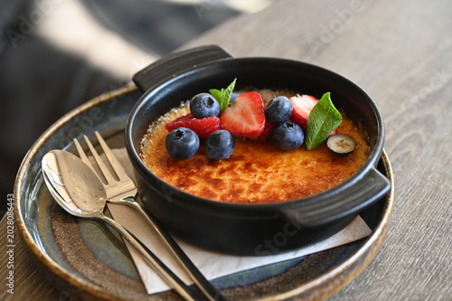 Fotografie French crème brûlée dessert with fresh fruit served in a black bowl