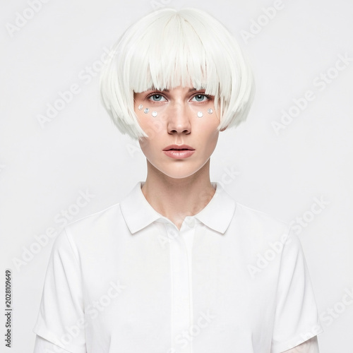 Futuristic young woman with short white bob haircut and creative face makeup posing in polo shirt against white background.