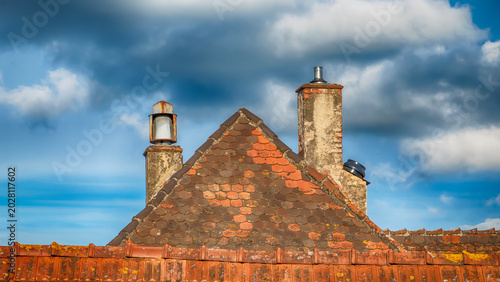 Old Weathered Roof with Clay Tiles and Two Chimneys Against Dramatic Cloudy Sky, Germany