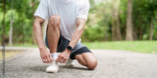 Asian man tying shoelace in park, preparing for outdoor fitness run