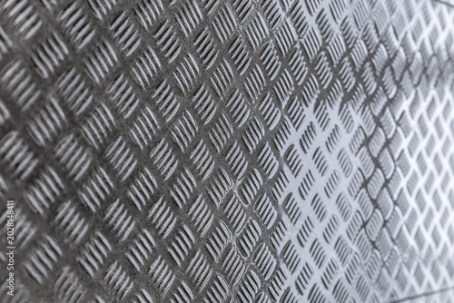 Close-up of gray diamond plate metal surface with raised tread pattern, industrial texture, shallow depth of field, and copy space