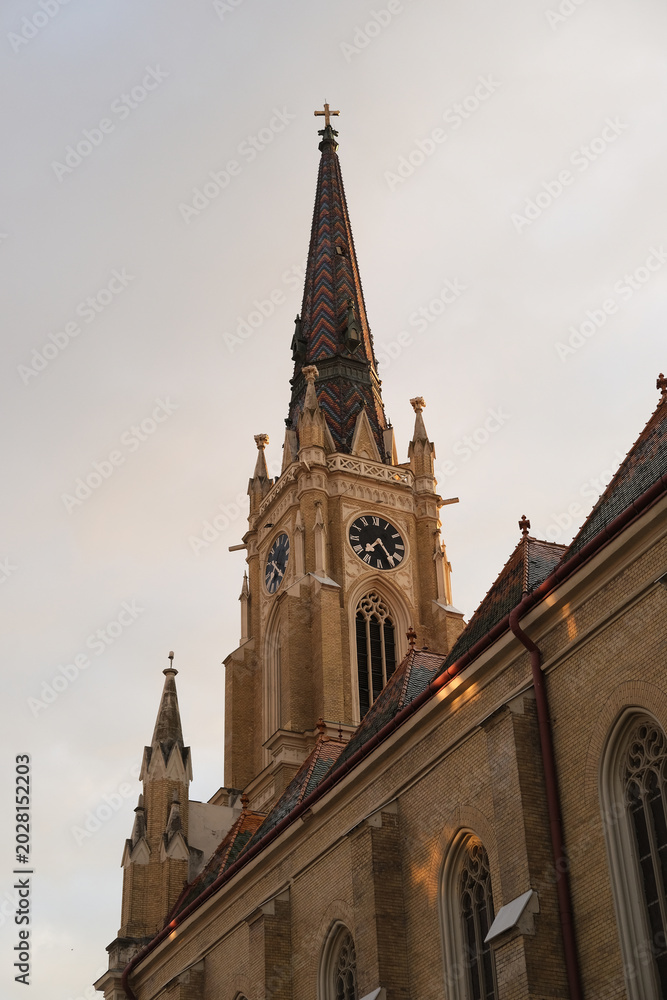 Fototapeta premium Church spire with clock tower, Gothic architecture in brick, ornate rooflines and sunset light on the exterior