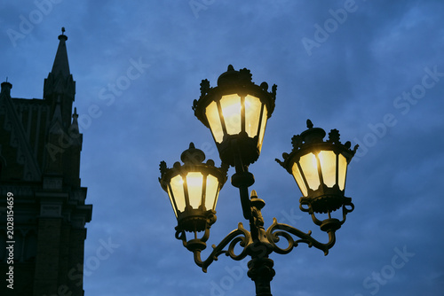 Foto Ornate streetlight with metal lanterns glowing against a dusky blue sky, urban e
