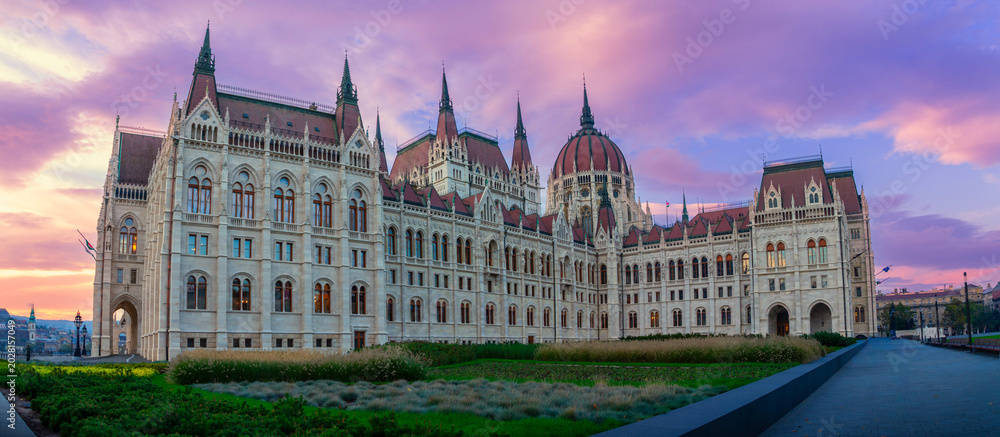 Fototapeta premium Hungarian parliament building on the danube in budapest at sunset, gothic revival spires and ornate facade glowing under a dramatic pink and purple twilight sky