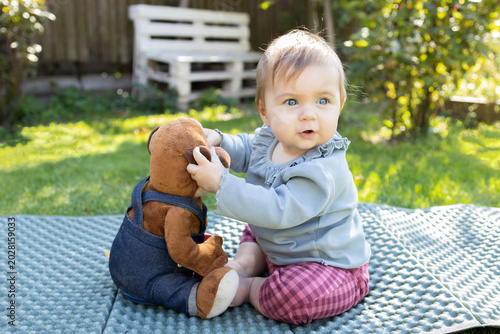 baby plays with a toy dog while sitting on the grass in a park. A child explores the world on a summer day. Real life, happy childhood, funny moments.