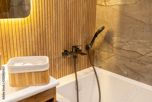 A modern bathroom shows wooden paneling with a shower head, stylish faucet, and a white tub ready for use in a home setting