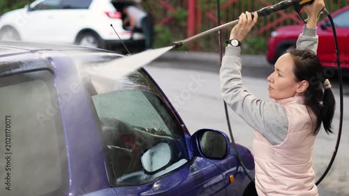 Experience the satisfaction of a fresh car wash as a woman enthusiastically cleans her blue car. The foam and water create a stunning visual, making even a mundane task enjoyable. Slow motion 4k video