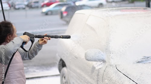 Join a woman as she takes pride in applying washing foam to cleaning her car at a self-service wash. The bright blues and foamy suds create an eye-catching contrast that enhances this everyday ritual.