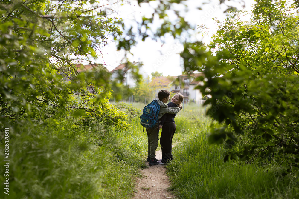Obraz premium Girl and a boy with school backpack on green path on way home from school. Authentic candid moment of friendship captured on the way home from school on a sunny spring day. 