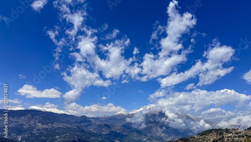 Schilderij op canvas Wide mountain range under vivid blue sky with scattered white clouds, distant pe
