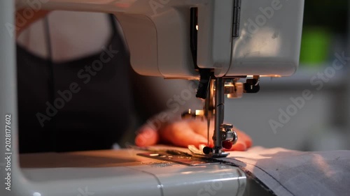 Hands carefully sew blue fabric with a machine, guiding it steadily under the needle. The close-up captures the rhythmic motion and precision required to create perfect, even stitches.