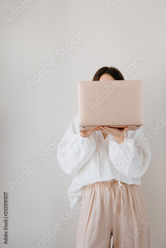 Young woman using laptop as face shield in aesthetic minimalist studio setting