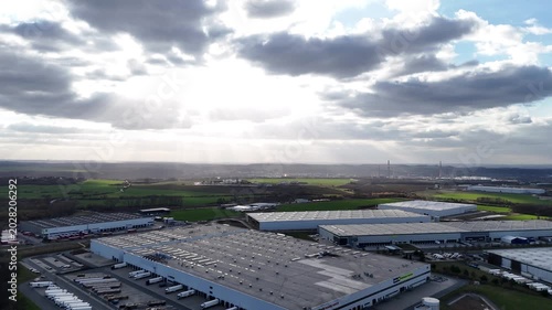 The aerial view in  captures an industrial park where sunbeams break through dramatic clouds. This scene highlights the contrast between logistical infrastructure and natural light.