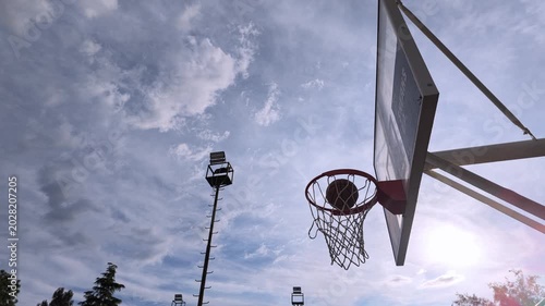 Slow motion footage of a basketball perfectly swishing through the hoop on a beautiful spring day. Blue sky, soft clouds, and the movement of the net create a dynamic and cinematic sports atmosphere. 