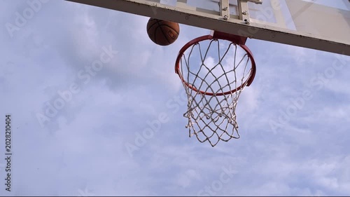 Slow motion footage of a basketball perfectly swishing through the hoop on a beautiful spring day. Blue sky, soft clouds, and the movement of the net create a dynamic and cinematic sports atmosphere. 