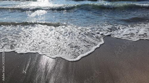 Slow motion close-up of ocean waves gently washing onto a sandy beach during sunset. Golden sunlight reflects across the water and wet sand, creating a calm and cinematic coastal atmosphere with relax
