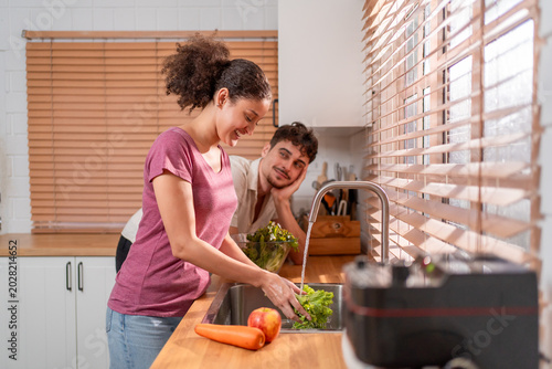 Hispanic Latina couple cleaning fresh vegetables for salad at the sink.