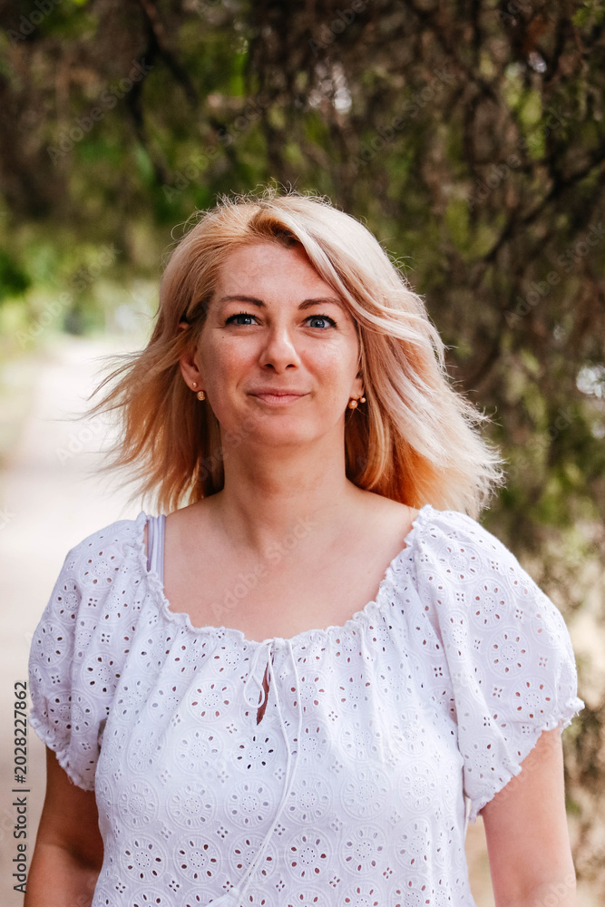 Naklejka premium A portrait of a positive, charming, and cheerful woman on a walk. A blonde woman in a white blouse looks at us. The blonde has a determined look. 